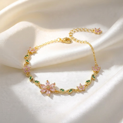 Gold bracelet with pink floral charms on a white fabric background
