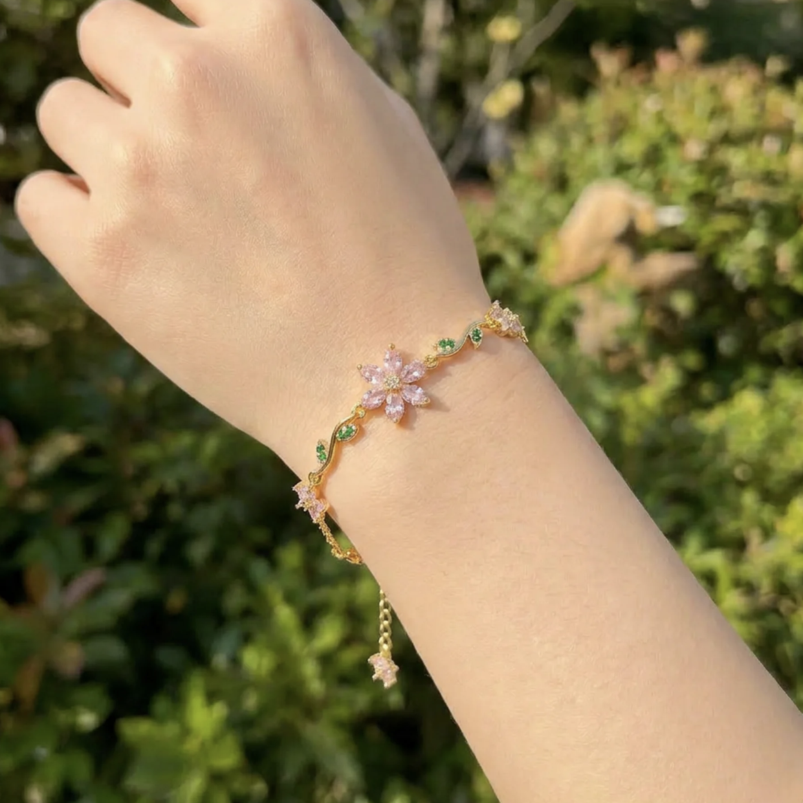 Hand wearing a delicate bracelet with floral designs against a blurred green background